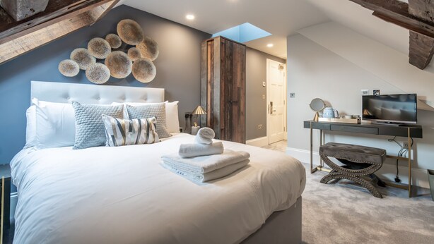 A bedroom with a large bed, a wooden wardrobe, a desk with a TV, and a skylight. - Old Abbey House Hotel (Abingdon)