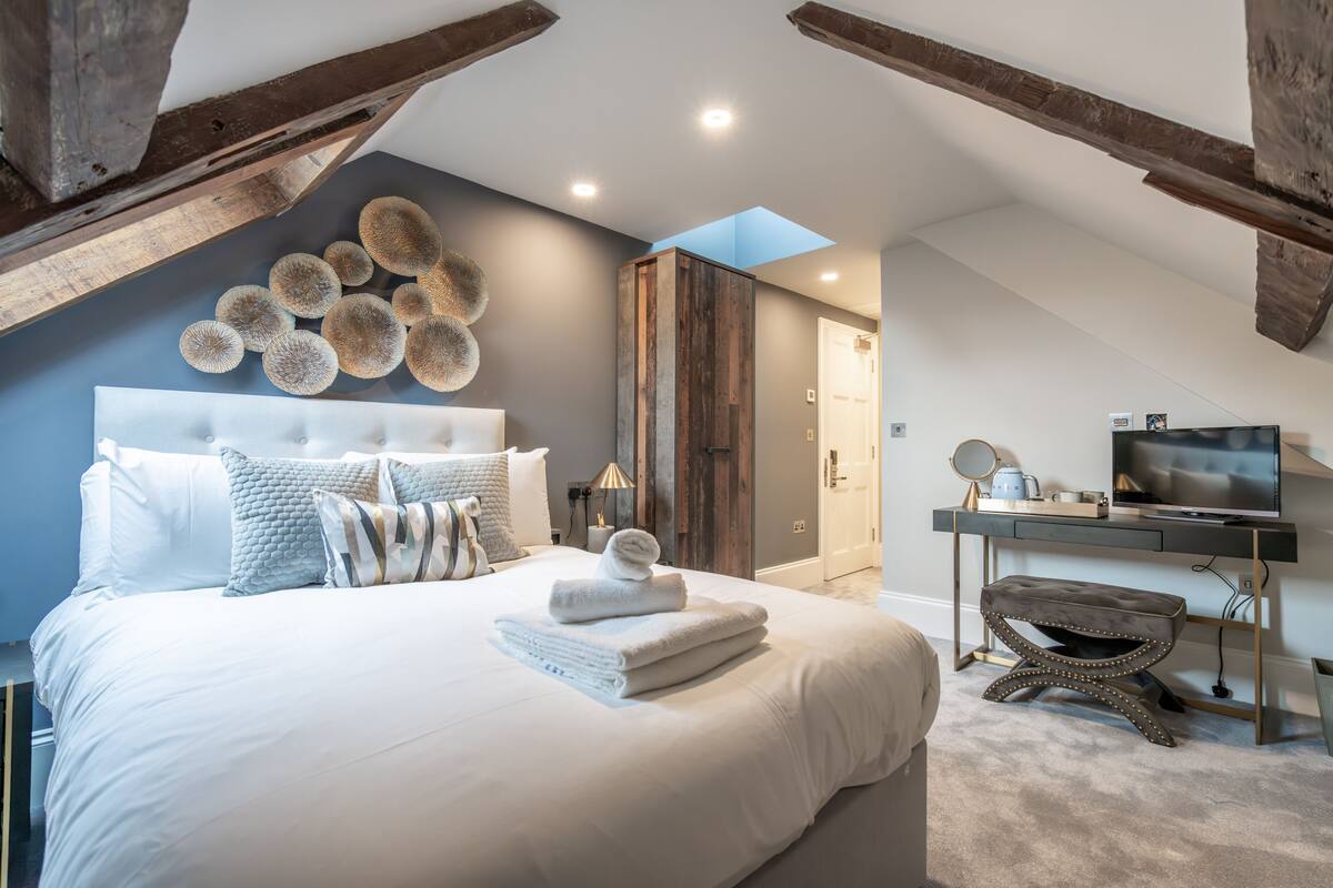Een slaapkamer met een groot bed, een houten garderobe, een bureau met een televisie en een dakraam.