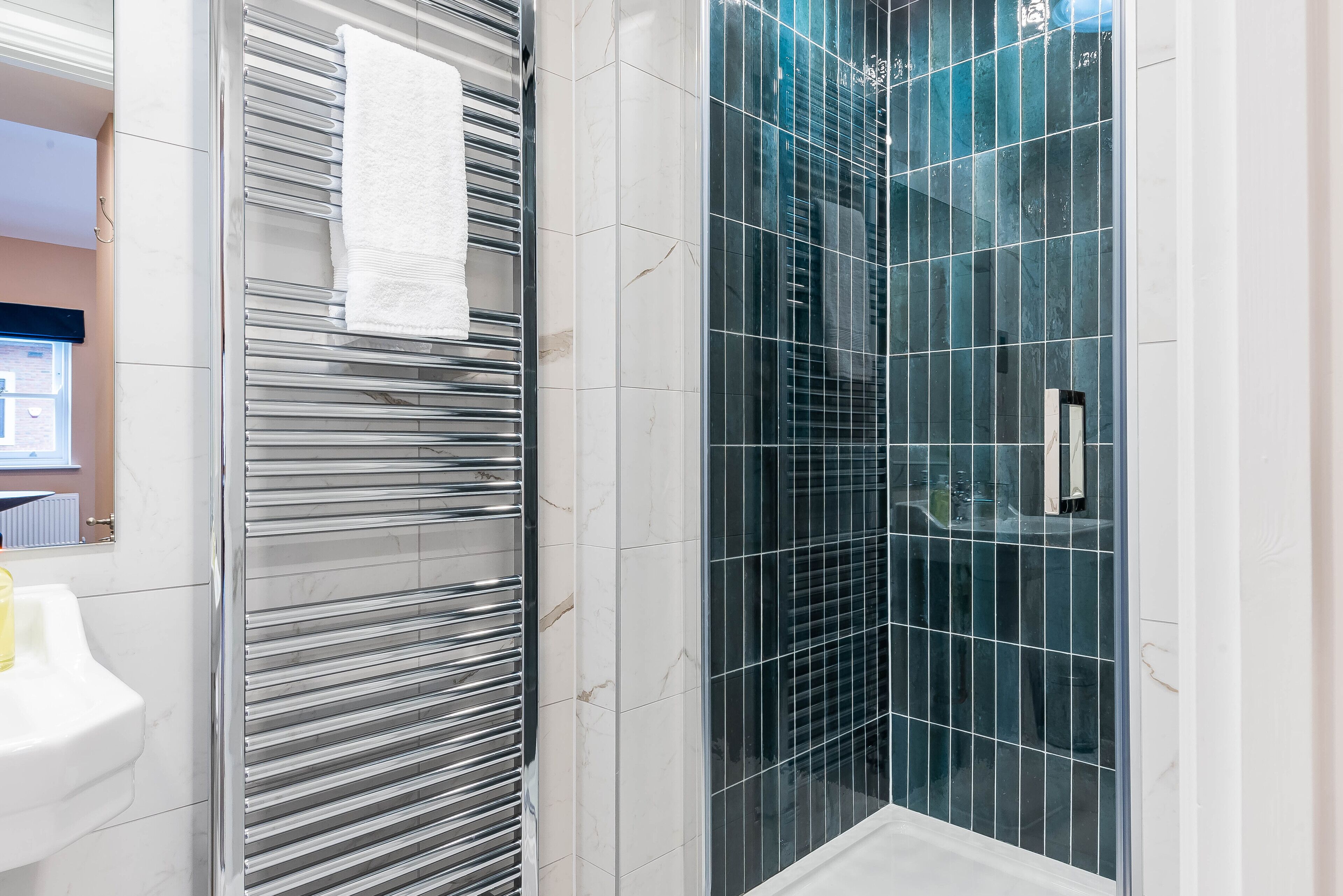 A modern bathroom with a glass shower enclosure, a white sink, and a towel rack.