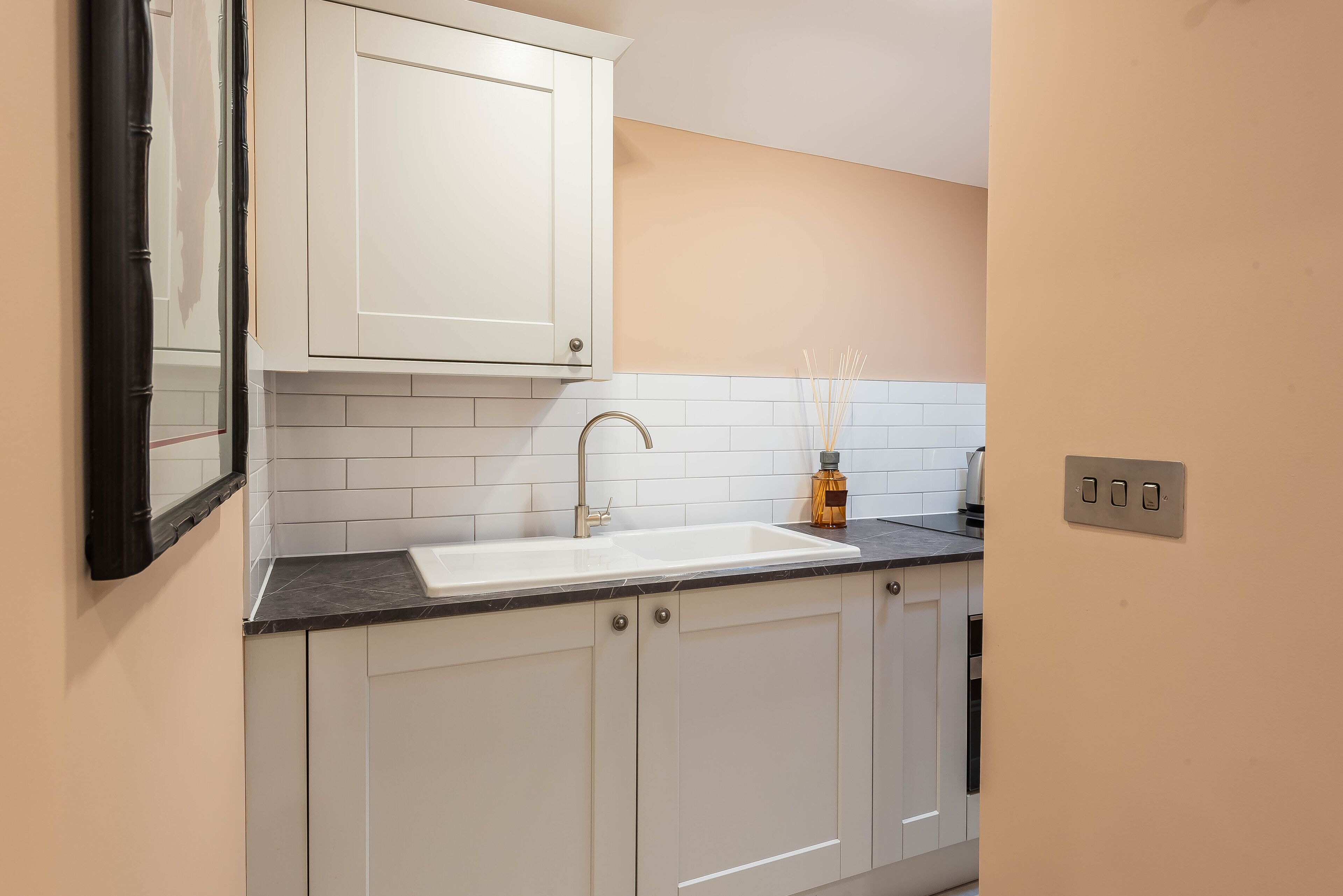 A kitchen with white cabinets, a white sink, a black countertop, and a mirror.