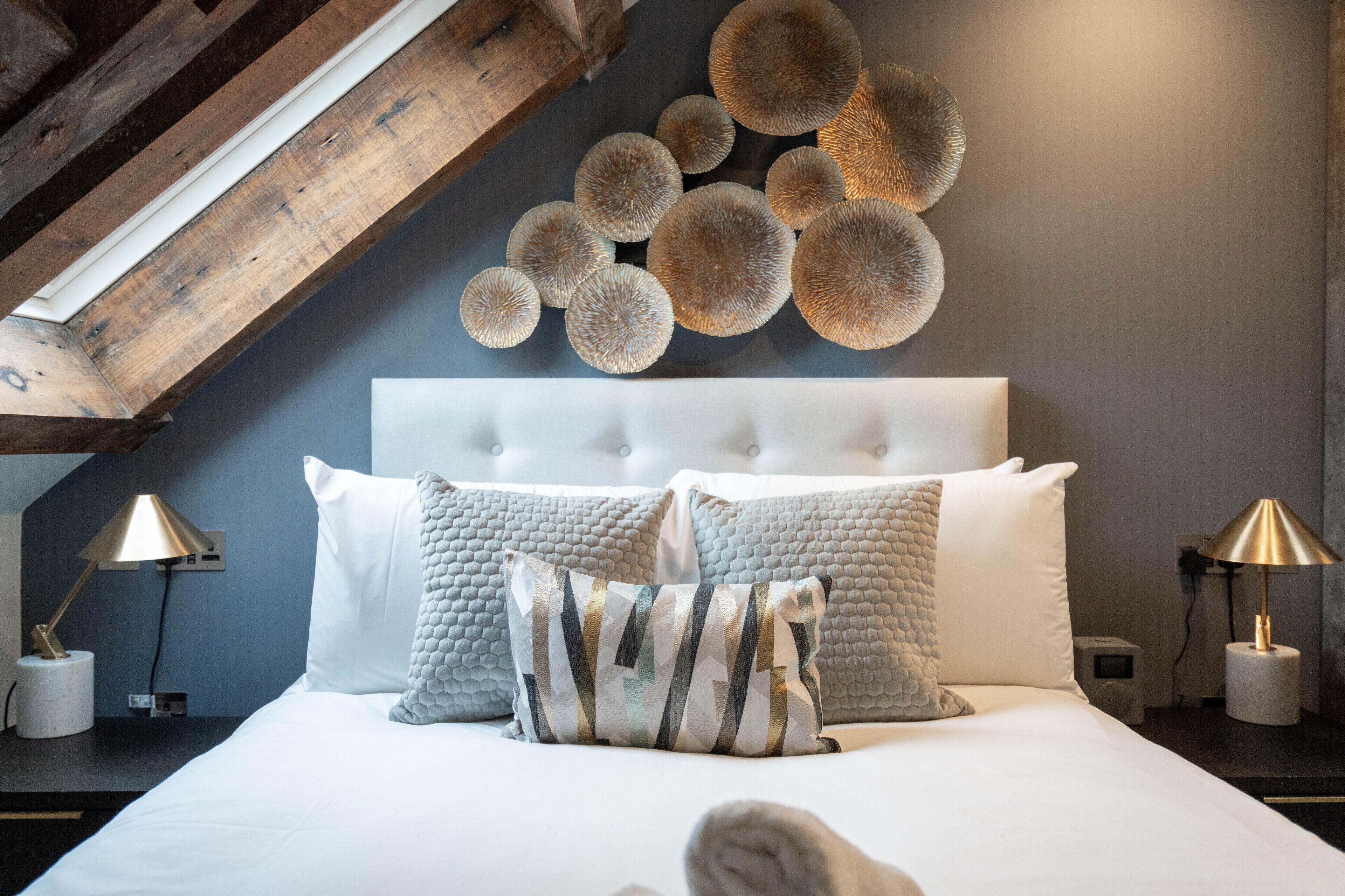 A bedroom with a tufted headboard, a large round wall decoration, and two bedside tables with lamps.