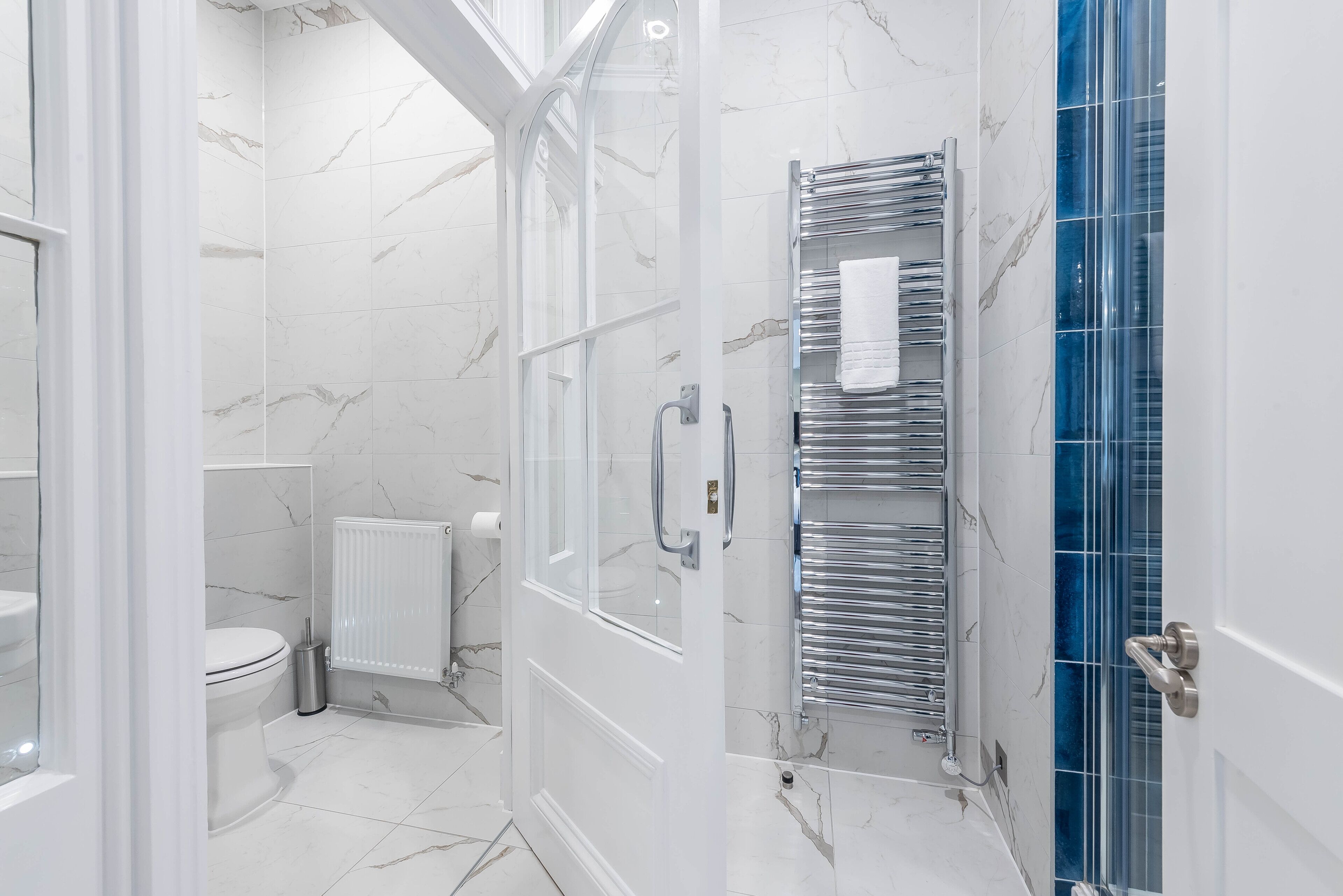 A modern bathroom with a glass shower enclosure, a white toilet, and a chrome towel rack.