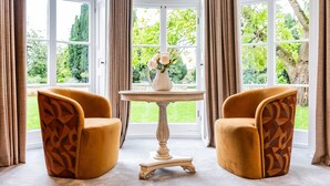 A room with two armchairs, a table with a vase of flowers, and large windows with curtains. - Old Abbey House Hotel (Abingdon)