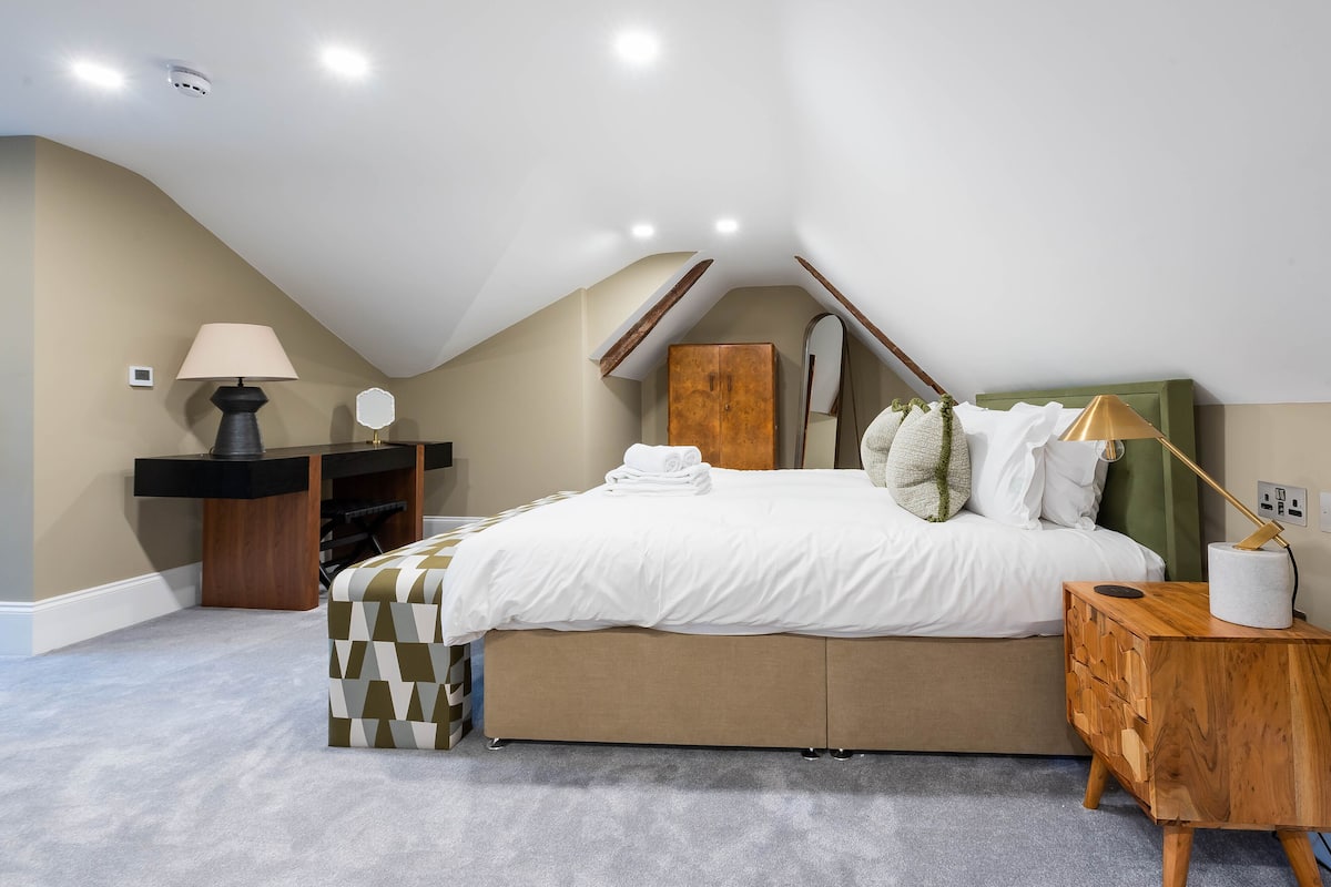 Een slaapkamer met een bed, nachtkastje, lamp en een houten garderobe.
