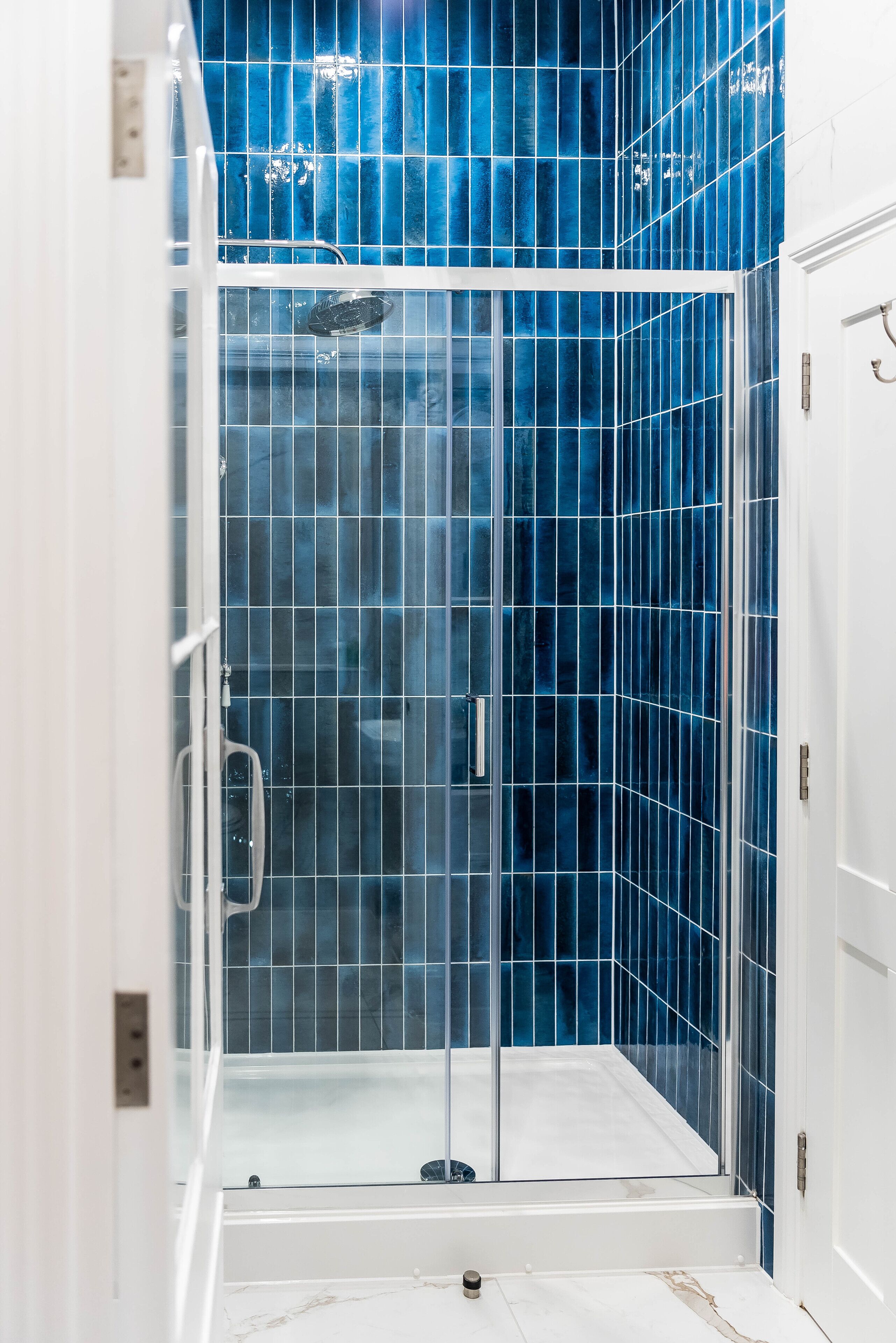 A glass-enclosed shower with a white door and a blue-tiled wall.