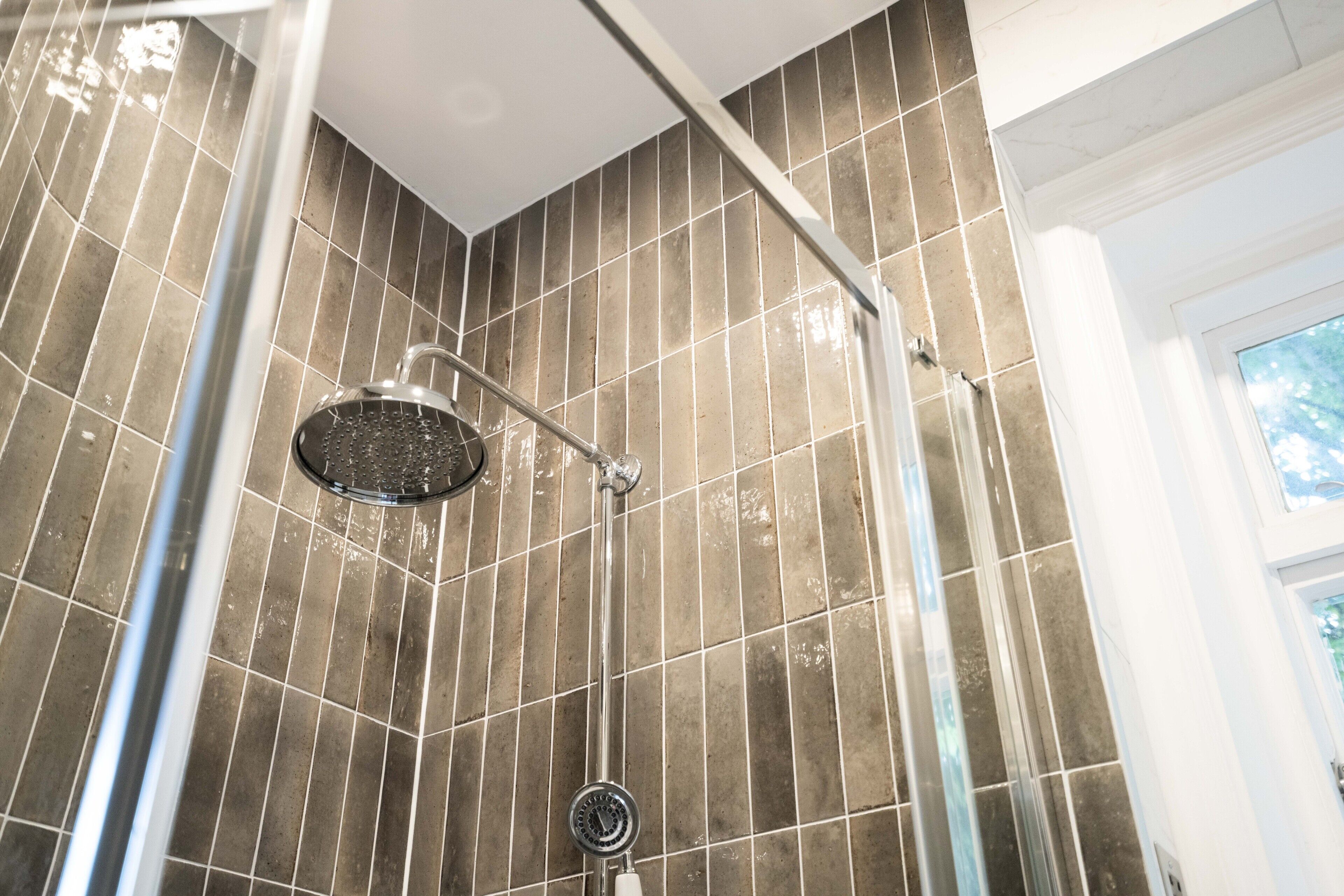 A shower with a handheld showerhead and a wall-mounted control panel.