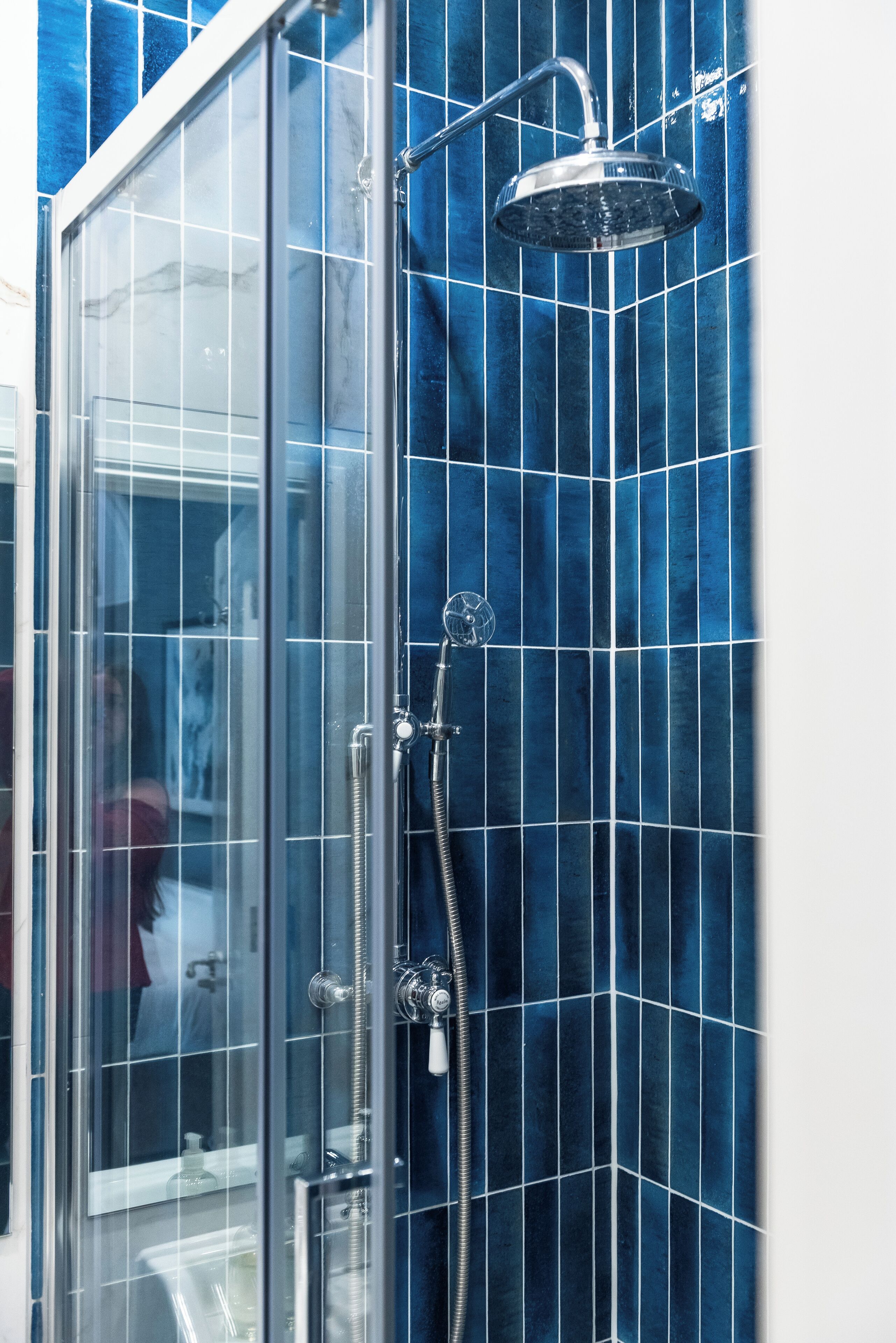A glass-enclosed shower with a handheld showerhead and a wall-mounted faucet.
