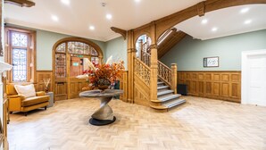 A spacious foyer with a wooden staircase, a round table with a vase of flowers, and a vintage sofa. - Old Abbey House Hotel (Abingdon)