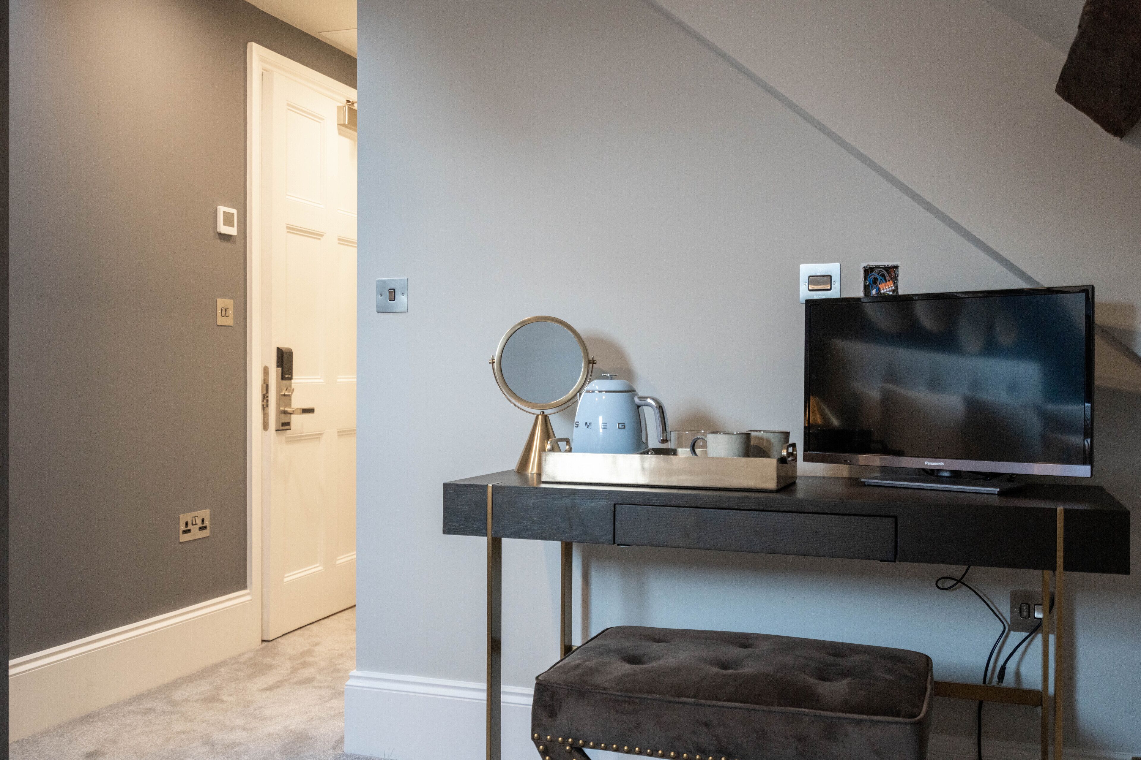 A modern bedroom with a bed, a desk with a computer, a TV, and a mirror.