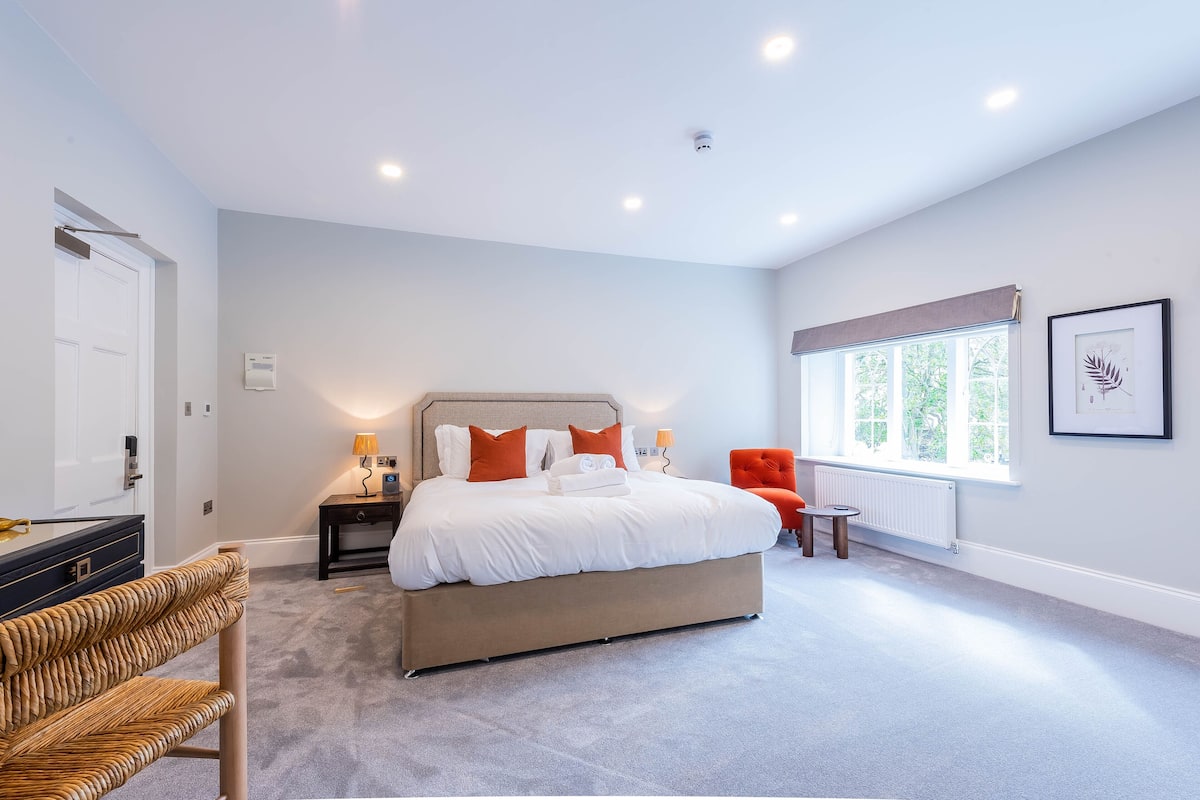 Een moderne slaapkamer met een groot bed, nachtkastjes, een stoel en een raam met uitzicht.