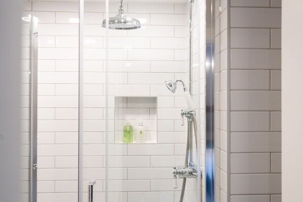 Zona de ducha con mampara de vidrio, ducha y estante con artículos de aseo.