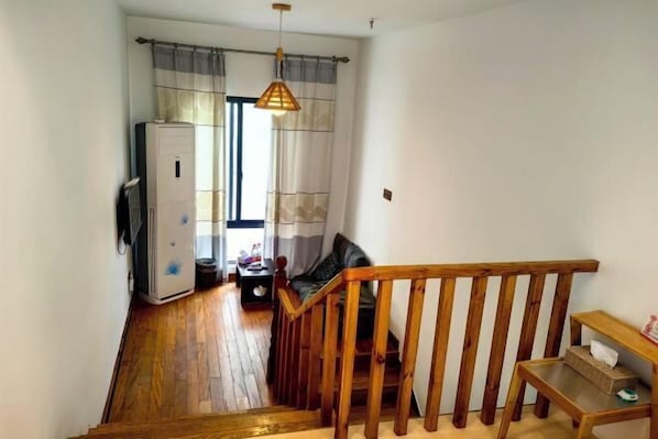 Um corredor estreito com piso de madeira, escada com corrimão de madeira, um sofá e uma mesa com um cesto.