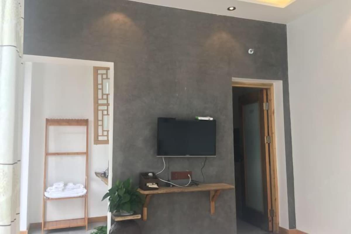 Quarto com televisão de tela plana presa a um console de madeira, porta-toalhas e uma porta que dá para outro cômodo.