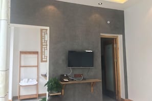 Quarto com televisão de tela plana presa a um console de madeira, porta-toalhas e uma porta que dá para outro cômodo.