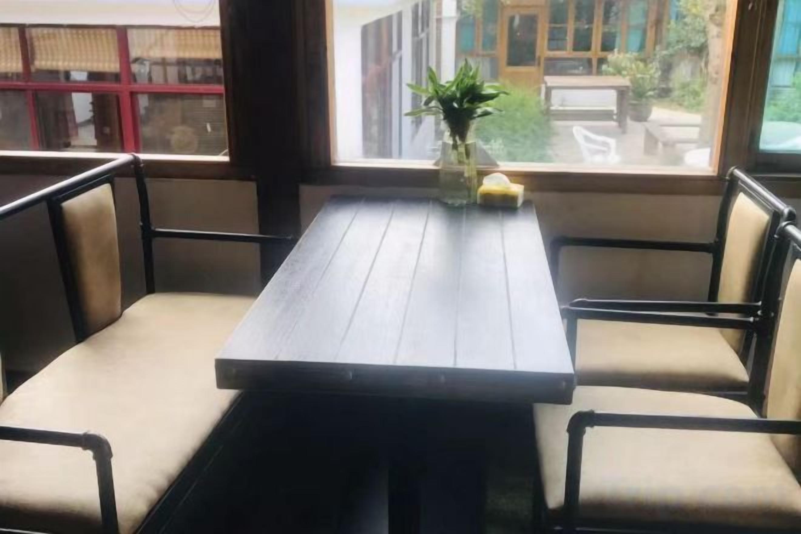 A rectangular table with chairs, a vase with a plant, and a window with a view of the outside.