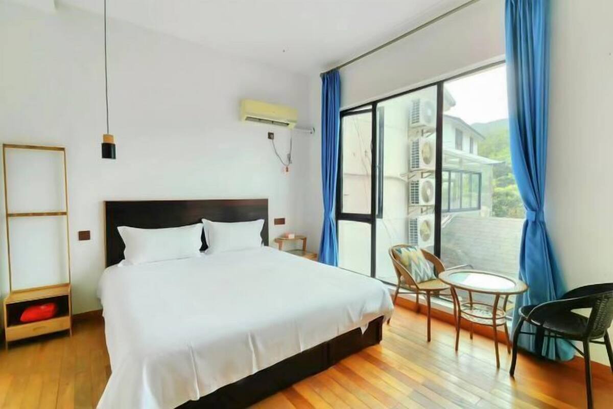 Una habitación de hotel con una cama, una mesita, una silla y un amplio ventanal con cortinas.