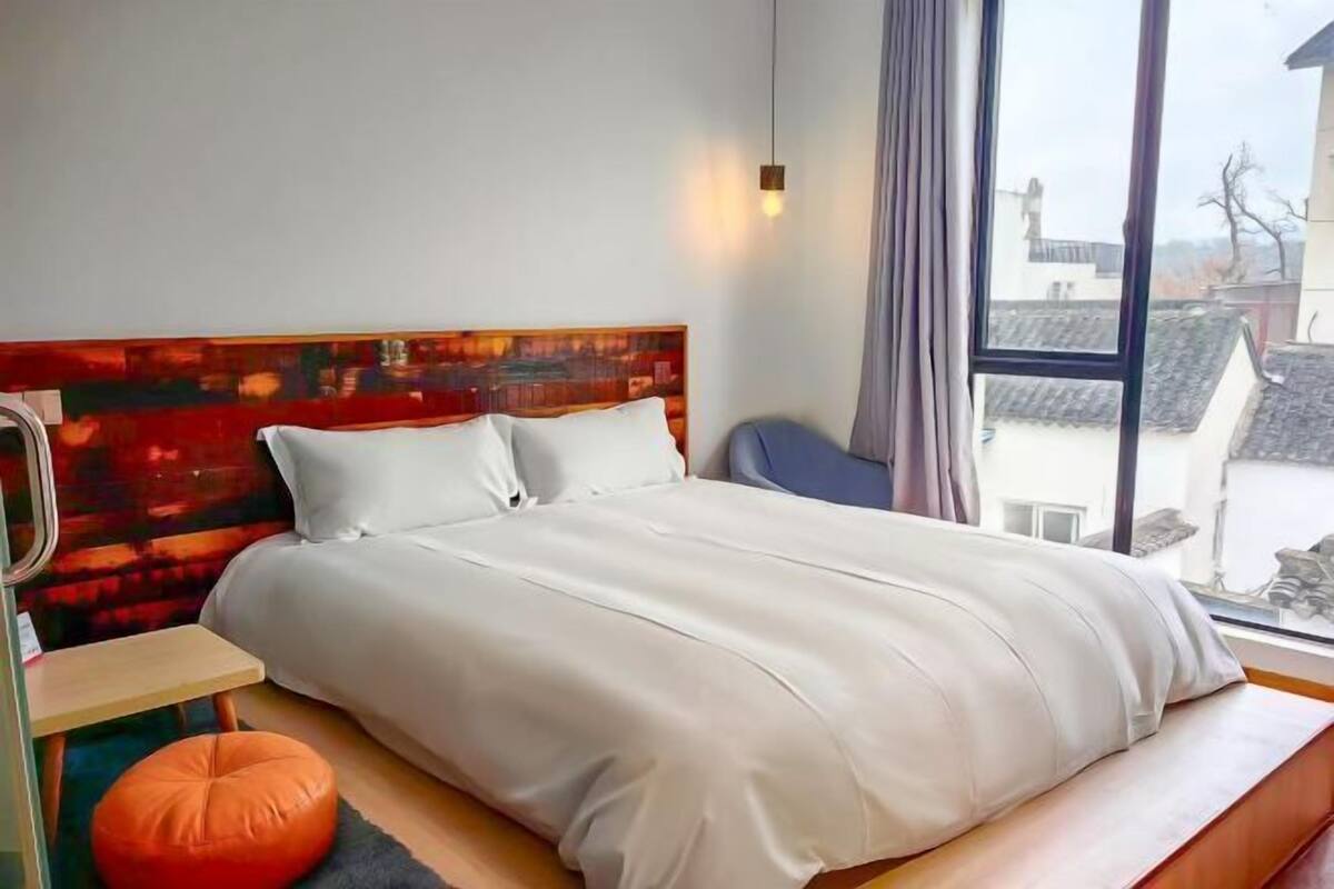 Un dormitorio moderno con una cama grande, una mesita y una ventana con vistas a edificios.