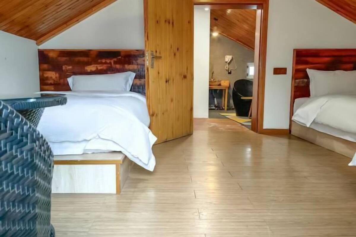 Un dormitorio con dos camas, techo de madera y un baño a la vista.