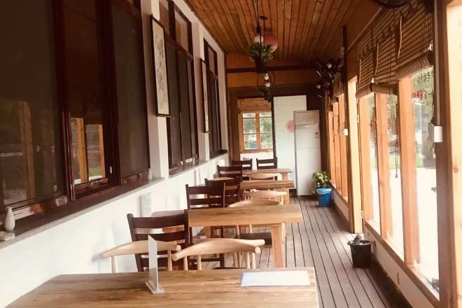 An indoor dining area with wooden tables and chairs, large windows, and a wooden ceiling.