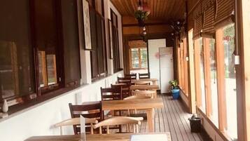 An indoor dining area with wooden tables and chairs, large windows, and a wooden ceiling.