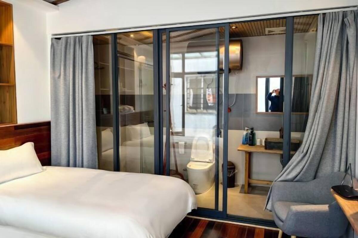 Una habitación de hotel moderna con una cama grande, un área de descanso y un ventanal que da a un baño.