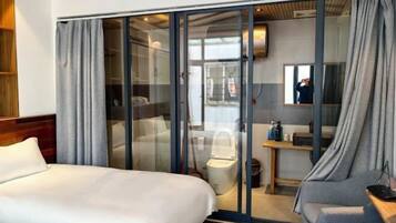 Una habitación de hotel moderna con una cama grande, un área de descanso y un ventanal que da a un baño.