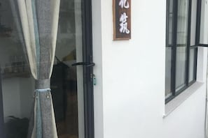 Uma porta com um letreiro em cima, uma janela e uma cortina cobrindo parcialmente a porta.