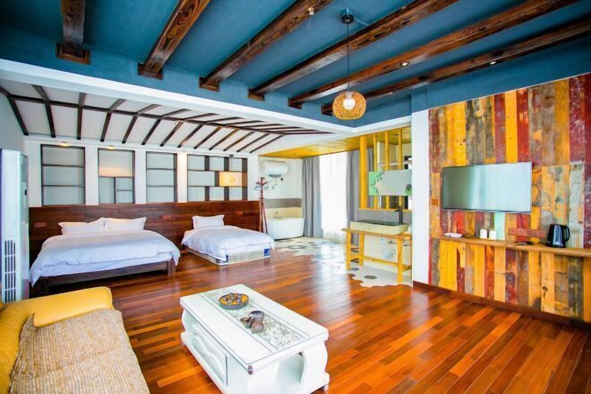 Habitación de hotel con dos camas, un sofá, una mesa de centro, un televisor y una pared colorida.