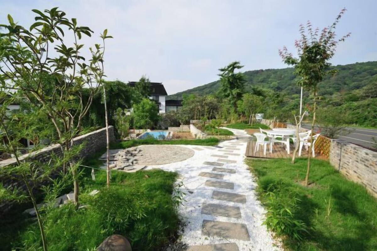 Un sendero que lleva a una casa con techo de tejas de piedra, rodeada de vegetación y una colina al fondo.