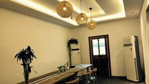 Una cocina con una mesa de madera, lámparas colgantes, un refrigerador y una puerta que da a otra habitación.