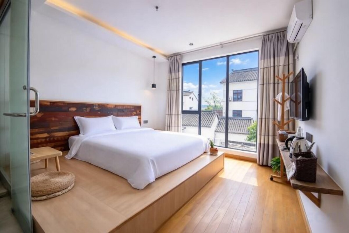 A bedroom with a bed, bedside table, and a view of the outside.