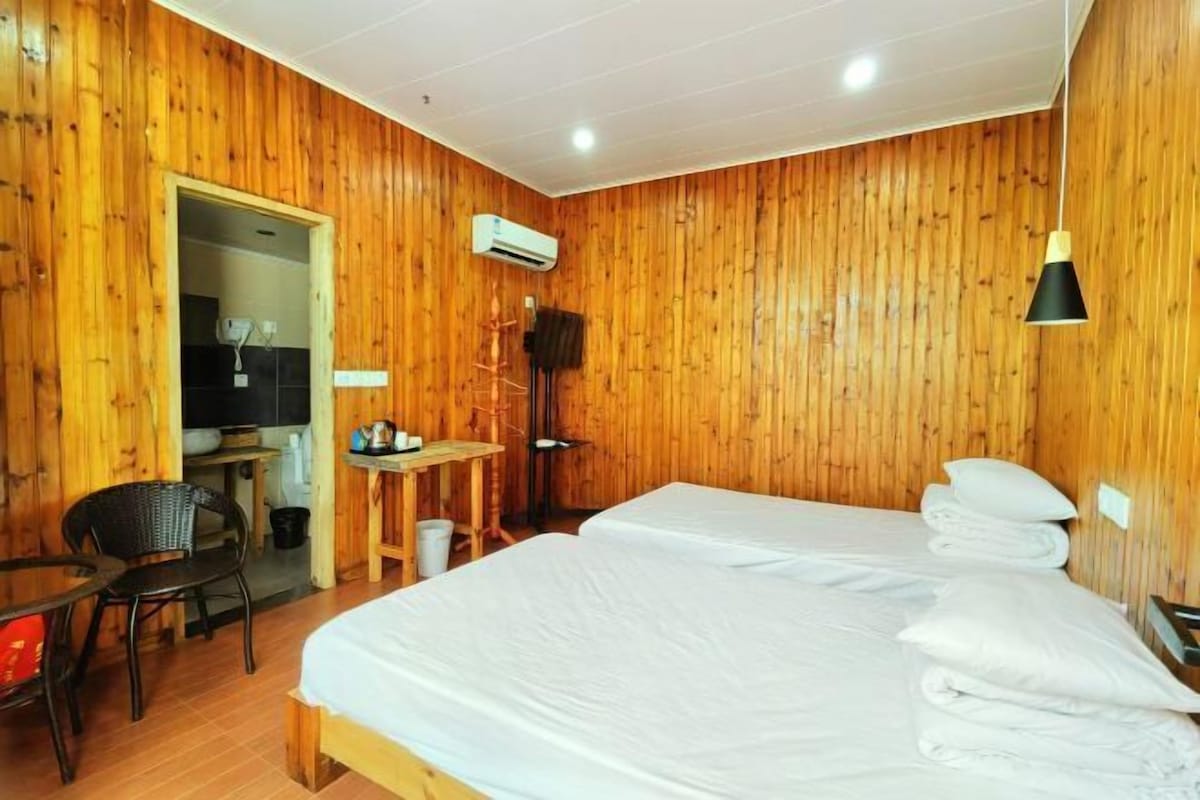 Quarto com painéis de madeira, duas camas, uma escrivaninha, uma cadeira e um aparelho de ar condicionado.