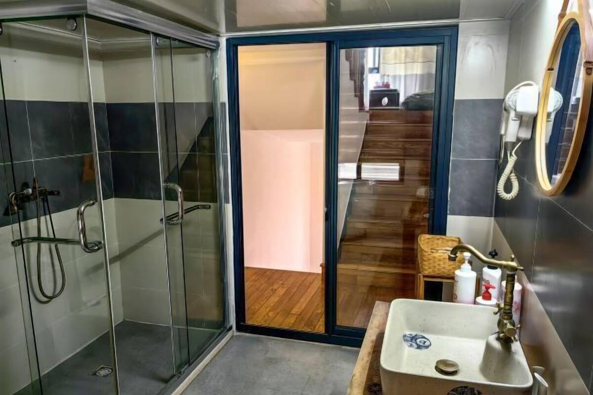 Un baño moderno con cabina de ducha de vidrio, tocador de madera y una escalera visible que conduce a otra habitación.
