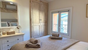 Ein Schlafzimmer mit einem großen Bett, einem Schminktisch, einem Spiegel und einem Fenster mit Blick auf einen Balkon.