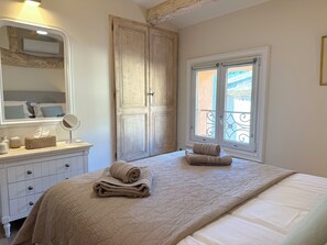 A bedroom with a large bed, a dresser, a mirror, and a window with a view of a balcony.