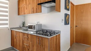 Cocina compacta con armarios de madera, horno microondas integrado y cocina a gas.