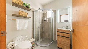 Un baño moderno con ducha de vidrio, inodoro, lavabo con espejo y estantes de madera con plantas.