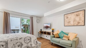 A bedroom with a bed, a light green sofa, a mounted TV, and a window with curtains. - 321 Getaway in Seattle Center-Belltown (Seattle)