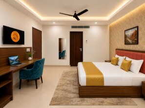 A hotel room with a bed, desk, chair, TV, and a ceiling fan. - Hotel The Heights (Haridwar)