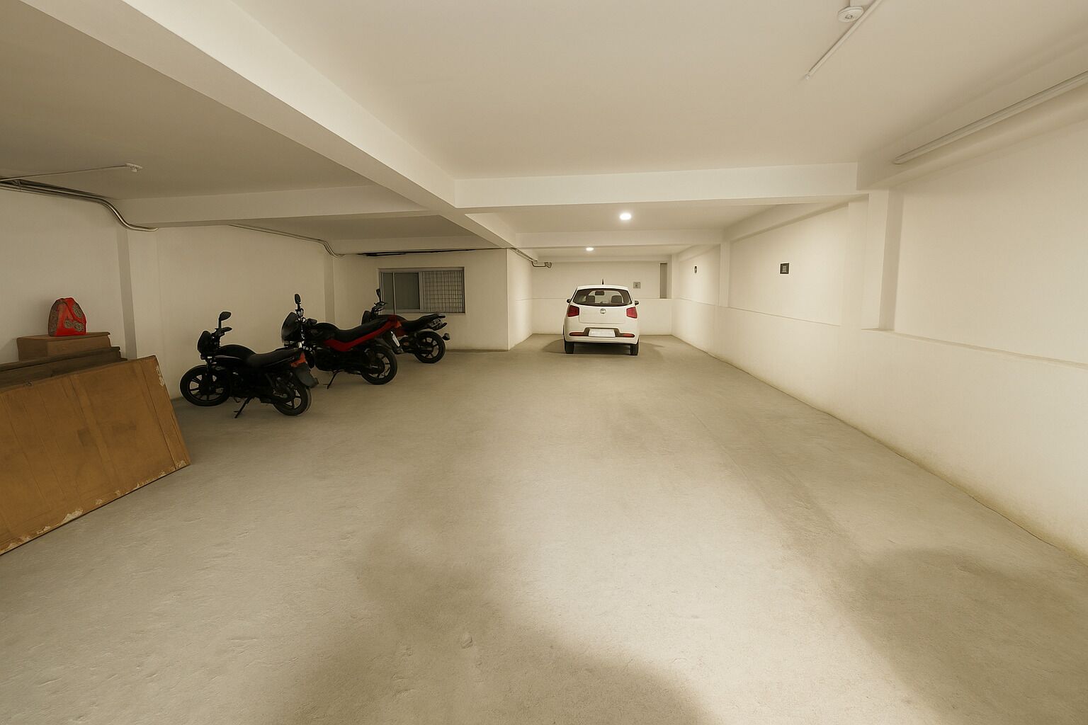 A spacious, well-lit garage with a concrete floor, two motorcycles, and a white car parked.