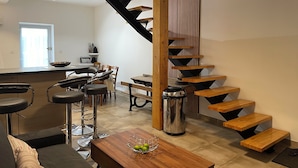 Een moderne keuken met een houten trap, een eethoek met barkrukken, en een koffieapparaat.