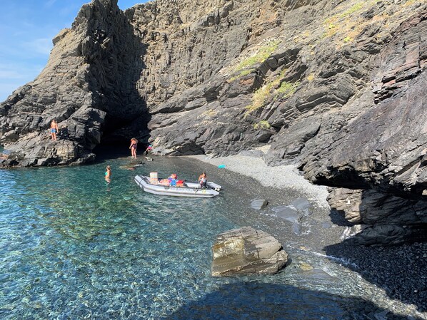 Una playa rocosa con agua cristalina, un bote y gente.