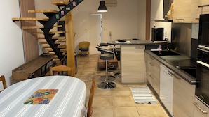 Een moderne keuken met een ingebouwde kookplaat, een eethoek met een geruit tafelkleed, en een houten trap met foto's.