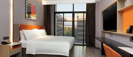 A modern hotel room with a large bed, a desk, a chair, a TV, and a window with a city view.