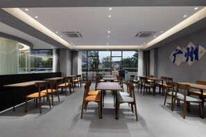 A modern dining area with tables and chairs arranged in rows, large windows providing natural light, and a view of the outside.
