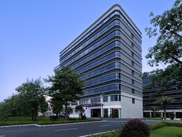 Un hôtel moderne à la façade incurvée, doté de plusieurs étages et d’un jardin bien entretenu.