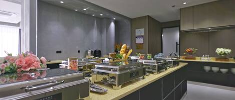 A modern kitchen with stainless steel appliances, a buffet setup, and decorative flowers.