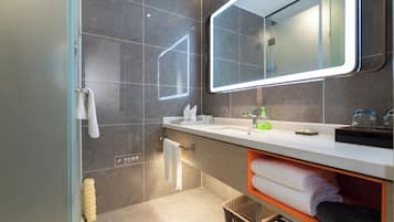 A modern bathroom with a glass shower enclosure, a large mirror, a white sink, and neatly folded towels.