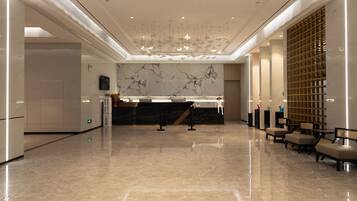 A spacious lobby with a marble reception desk, seating area, and a high ceiling with hanging lights.