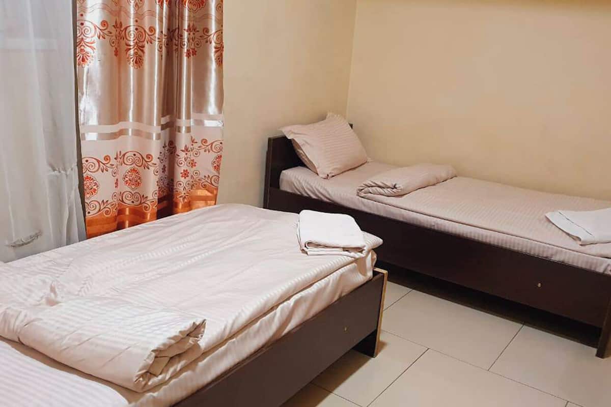 A room with two single beds, a curtain with a floral pattern, and a plain wall.